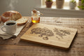 A rectangular bamboo cutting board with rounded corners, featuring a detailed laser-engraved design of a honeycomb, dripping honey drops, flowers, and a bee on a light beige background.