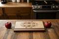 A rectangular wooden cutting board with a natural light wood center, dark brown end caps, and decorative stripes. The center features a laser-engraved floral design of sunflowers and the text 'Friends & Family Gather Here'.